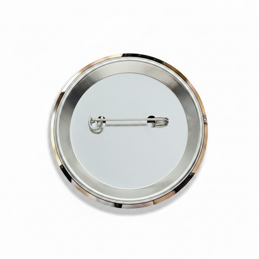 The back view of a round pinback button badge, showing a silver-tone metal rim, a white center, and a safety pin clasp mechanism.