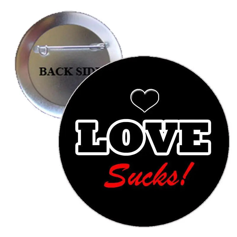 Black pinback brooch with white LOVE text, red “Sucks!” and small heart.