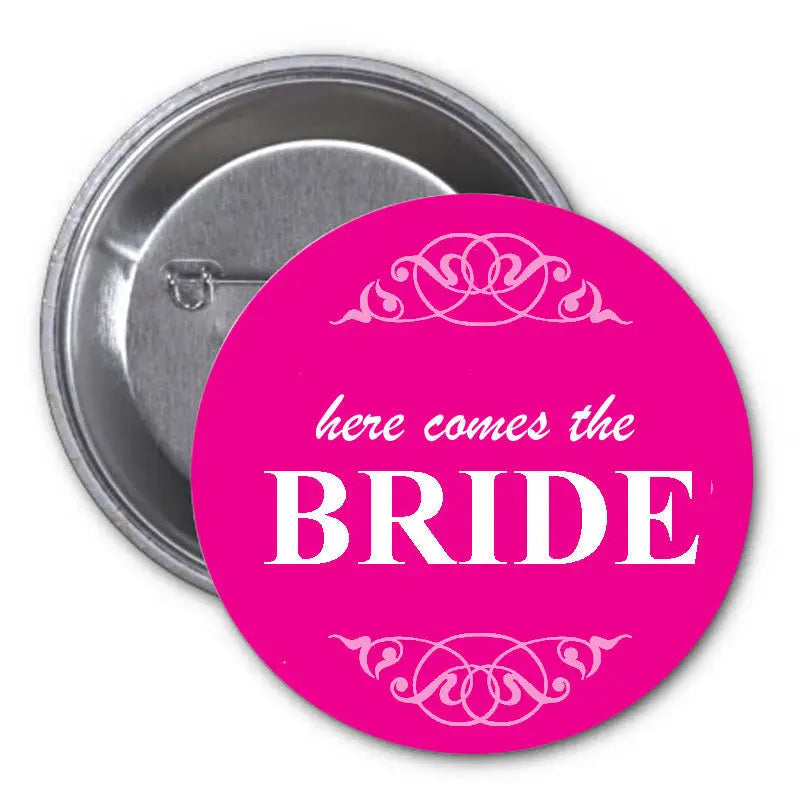 Pink pinback button with “Here Comes the BRIDE” text and floral heart design