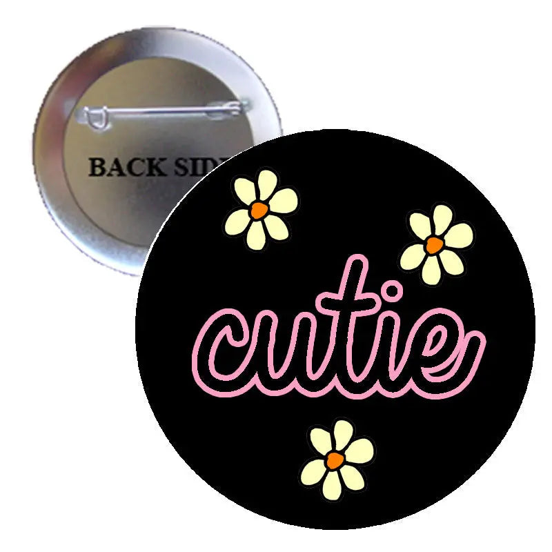 Cutie pinback button, black round badge with pink script and yellow daisy icons