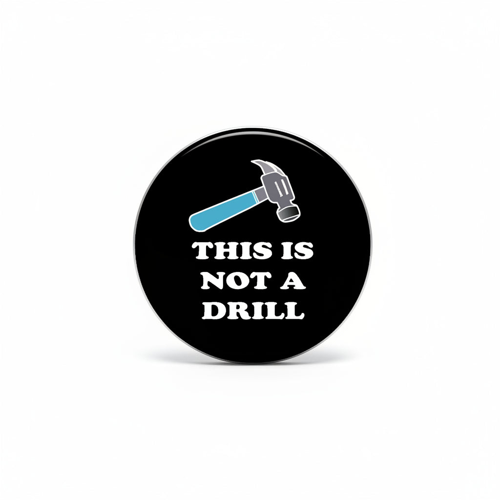 Round black pinback button with wrench graphic and text “THIS IS NOT A DRILL”.