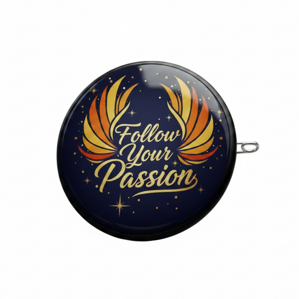 A round gold-tone pin or badge with a navy blue face, featuring orange and yellow wings and the words 'Follow Your Passion' in gold script, shown on a dark gray surface with part of a gold chain visible.