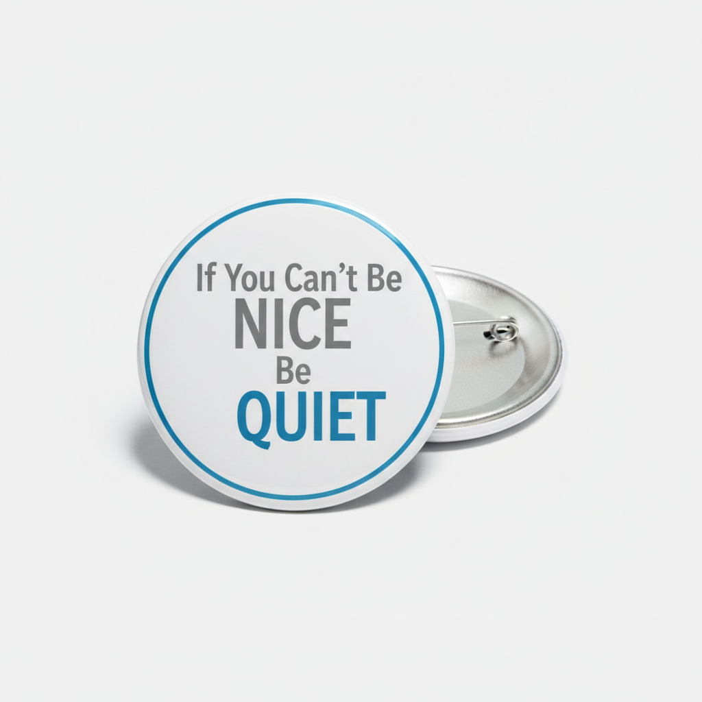 A round pin-back button badge with a white face, a thin blue border, and the text 'If You Can't Be NICE Be QUIET' in gray and blue lettering. A second badge is partially visible behind it, showing the silver metal back pin mechanism.