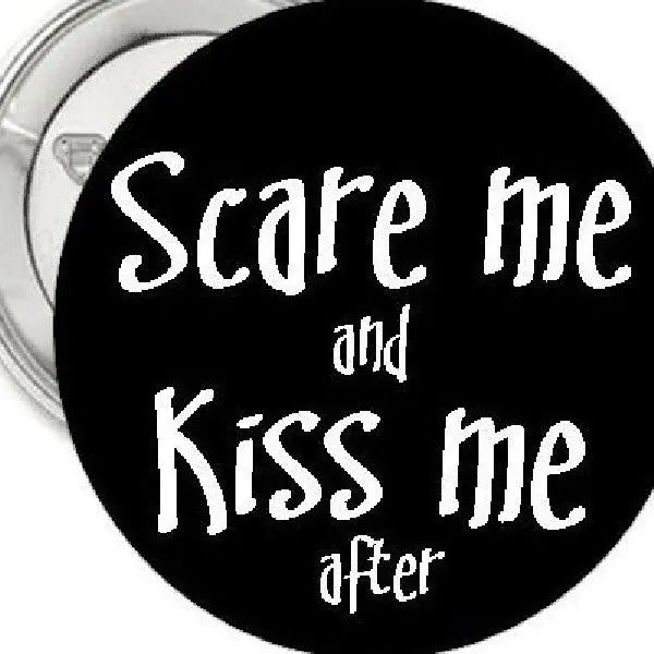 Black 1.25-inch pinback button with white 'Scare me' and 'Kiss me' text