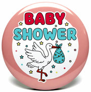 A round pink baby shower button badge featuring a white stork carrying a blue baby bootie and the words 'BABY SHOWER' in red and blue lettering.