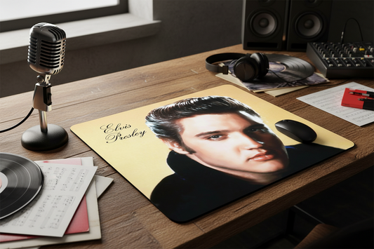 Desk setup with a mouse pad featuring Elvis Presley's face, microphone, records, and speakers.