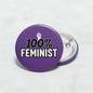 Purple 2.25-inch pinback button with "100% FEMINIST" text and metal back clasp