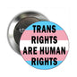 Round pinback button with colorful stripes and text: “TRANS RIGHTS ARE HUMAN RIGHTS”