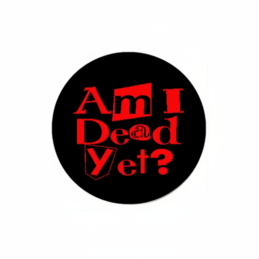 A circular black sticker or button featuring the text 'Am I Dead Yet?' in a stylized red font, centered on a plain white background.