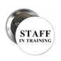 Round silver pin with white face: STAFF IN TRAINING