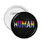 Round pin badge, black face with multicolor "HUMAN" text and metal back clasp