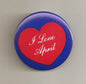 Round blue pinback button with red heart reading 'I Love April'
