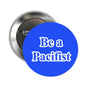 Round silver pinback brooch with dark center and 'Be a Pacifist' text