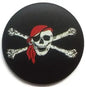 Round black Jolly Roger pin badge with skull, red hat, and crossed bones design