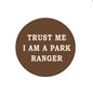 Brown circular park ranger pinback button with white text: “TRUST ME I AM A PARK RANGER”
