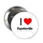 Round metal pinback brooch with “I” text and red heart next to “Fayetteville”
