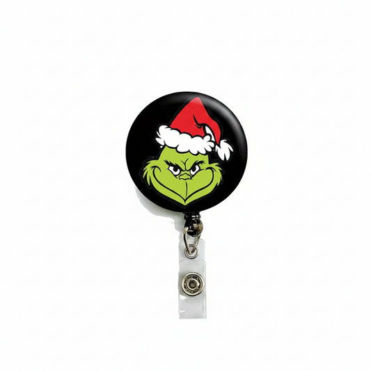 Retractable badge reel with round black face and green mascot in red Santa hat