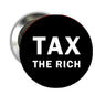 Round black pinback button badge with white 'TAX THE RICH' text and silver back