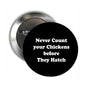 Round black pinback button with silver back; white text: 'Never Count your Chickens before They Hatch'.