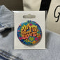 2.25-inch round collectible pin with colorful peace, love, and heart design on card