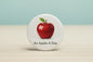 Round white enamel pinback button with red apple and 'An Apple A Day' text