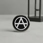 2.25-inch round pinback button with black background and white anarch symbol