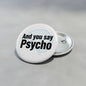 Round white pinback button: black 'And you say Psycho' text with metal back