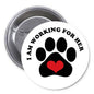 Round pinback button with black paw print, red heart, and “I AM WORKING FOR HER” text