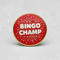 Red Bingo Champ pinback button with gold rim and white 'BINGO CHAMP' lettering