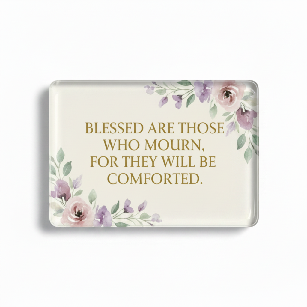 A rectangular glass or acrylic plaque with rounded corners, featuring the quote 'BLESSED ARE THOSE WHO MOURN, FOR THEY WILL BE COMFORTED.' in gold lettering, decorated with watercolor-style pink and purple flowers and green leaves in the top right and bottom left corners, shown on a clean white background.