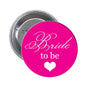 Pink round Bride to be pinback button with white script and heart; silver metal back.