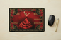 A rectangular desk mat with a romantic red and black tango illustration, displayed on a light wood desk alongside a black computer mouse and a gold pen.