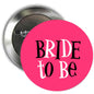 Round pink pinback badge with black “BRIDE TO BE” text