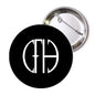 Round pinback button with black face, white monogram, and silver metal back with pin