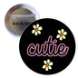 Cutie pinback button, black round badge with pink script and yellow daisy icons