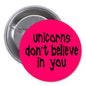 Pink round pinback button with black text: unicorns don't believe in you