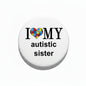 Pin-back badge, white circle with black rim, puzzle-heart I ♥ MY autistic sister text