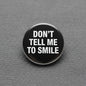 2.25-inch round pinback button with black face and white text: "DON'T TELL ME TO SMILE"