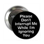 1.25-inch pinback button with black face and white text: Please Don't Interrupt Me...