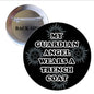 Round black pinback button with white 'My Guardian Angel Wears a Trench Coat' text
