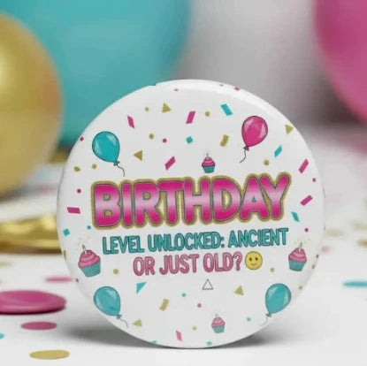A round white button or badge with colorful birthday graphics and the text 'BIRTHDAY LEVEL UNLOCKED: ANCIENT OR JUST OLD?' centered on a festive confetti and balloon background.