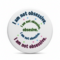 Round pinback button featuring multicolor text pattern with “I am not obsessive”