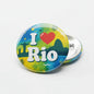 Rio pinback button with colorful globe art and a red heart, silver metal back
