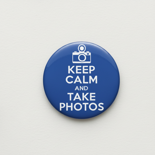 A round blue button pin with a white camera icon and the text 'KEEP CALM AND TAKE PHOTOS' on a light gray background.