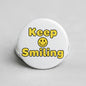 Keep Smiling pinback button, white with yellow text and smiling face graphic