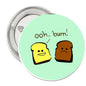 Round mint-green pinback button with cartoon bread faces and “ooh... burn!”