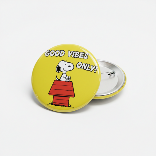 Two round pinback buttons on a light gray background. The front button is bright yellow with the text 'GOOD VIBES ONLY!' above a cartoon dog sitting on a red doghouse.