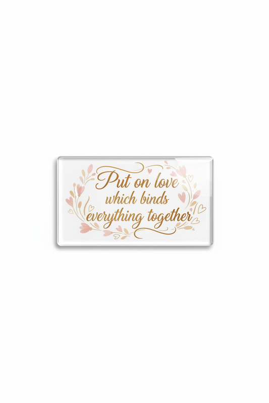 A rectangular clear acrylic block with rounded corners featuring the quote 'Put on love which binds everything together' in gold cursive, surrounded by a delicate pink floral wreath, on a plain white background.