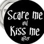 Black 1.25-inch pinback button with white 'Scare me' and 'Kiss me' text