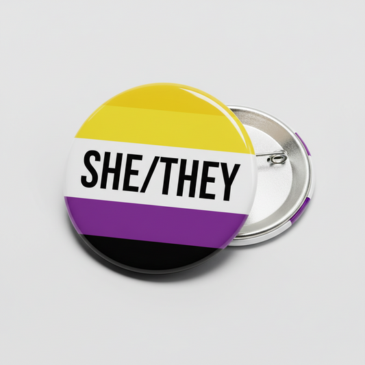 Non-binary pinback button with SHE/THEY text, flag stripes in yellow, purple, black